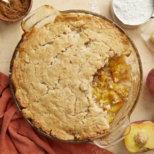 Overhead shot of peach cobbler with a scoop taken out in a glass pie plate.