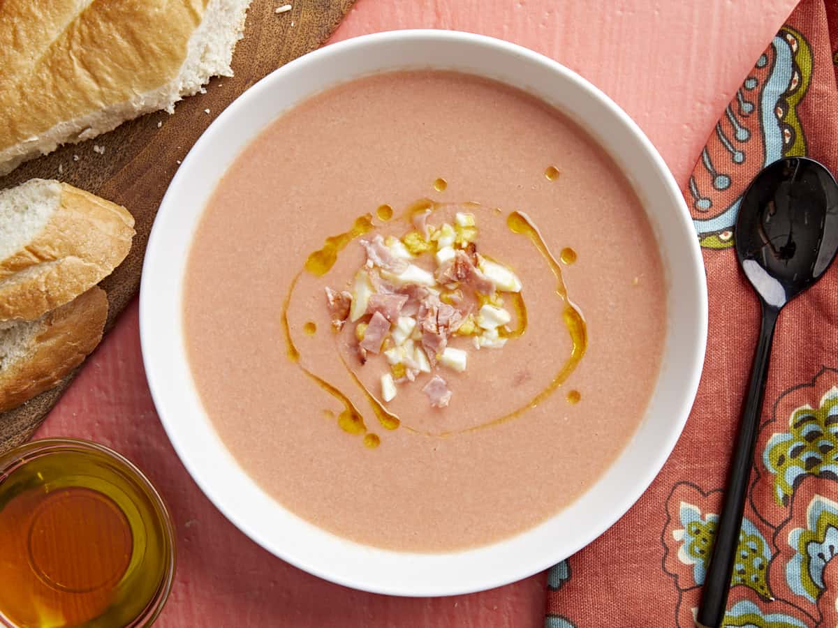 Overhead shot of a white bowl of Salmorejo garnished with a drizzle of olive oil, chopped hard-boiled eggs, and crispy ham crumbles.