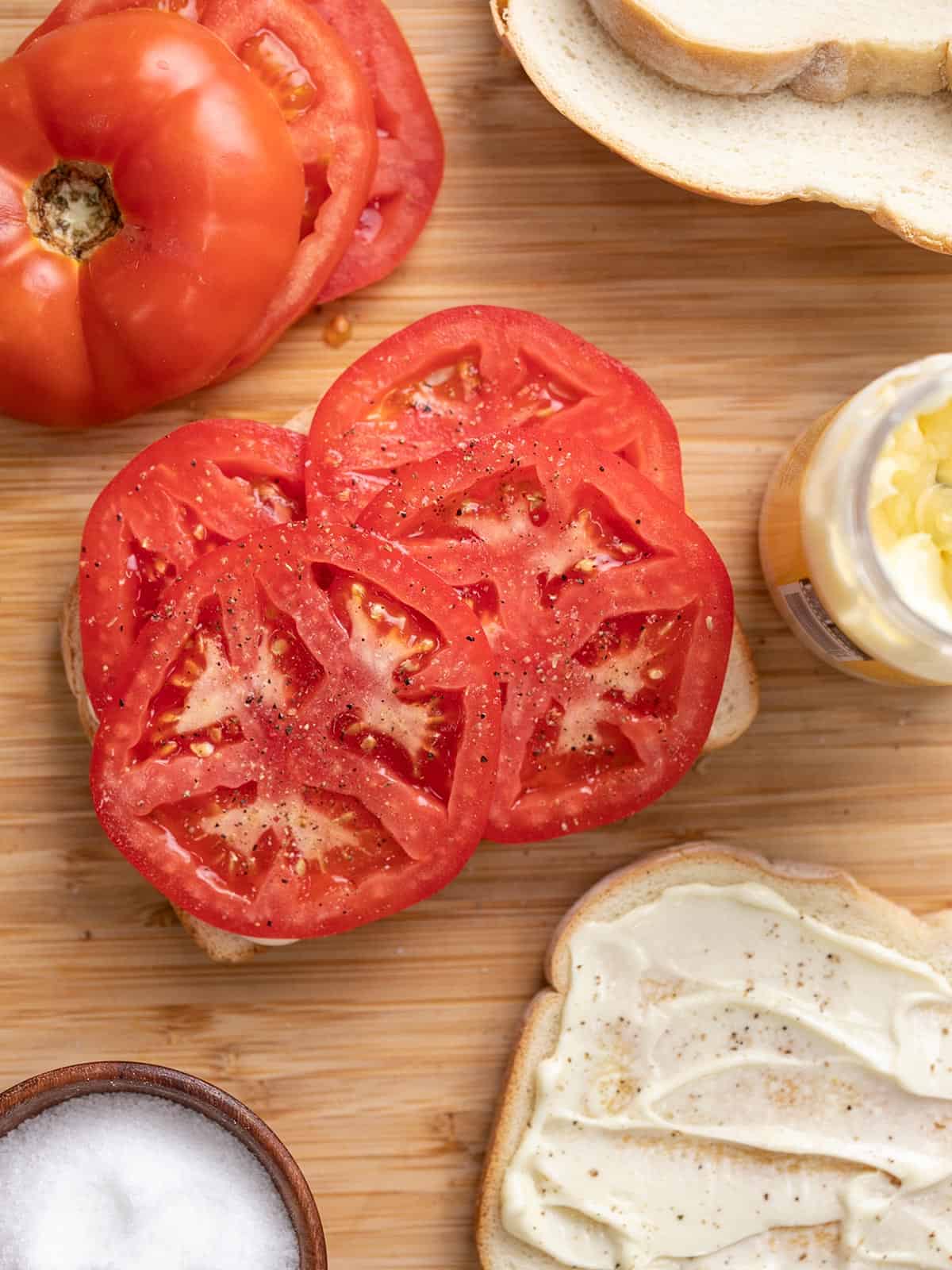 Tomato Sandwiches being built on a wooden cutting board.