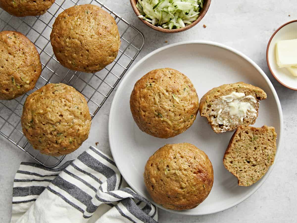 Zucchini muffins plated with one cut open and butter spread in the middle.