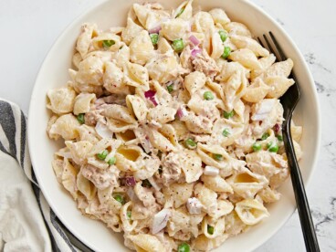 Plate of colorful tuna pasta salad garnished with peas, onions and a dressing.