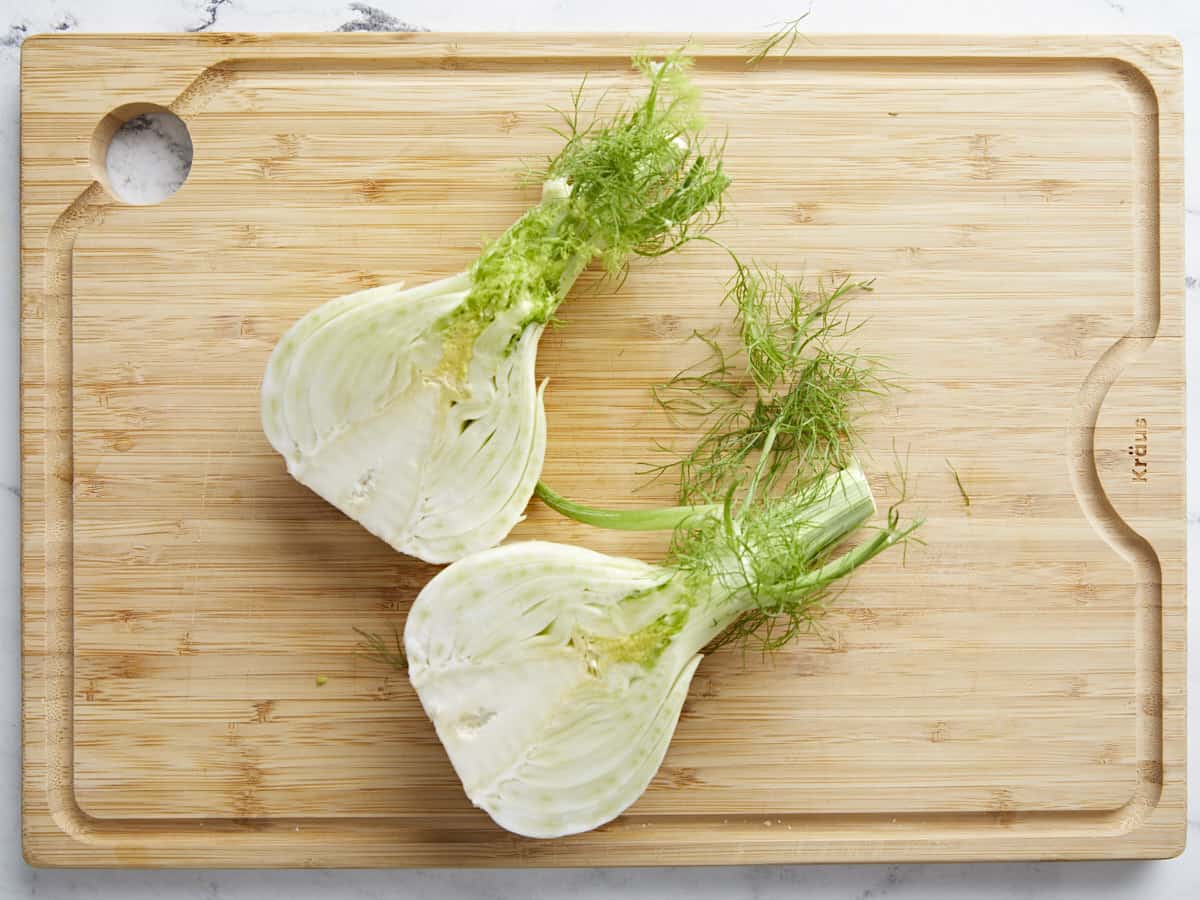 Overhead shot of a fennel bulb sliced in half on a wood cutting board.