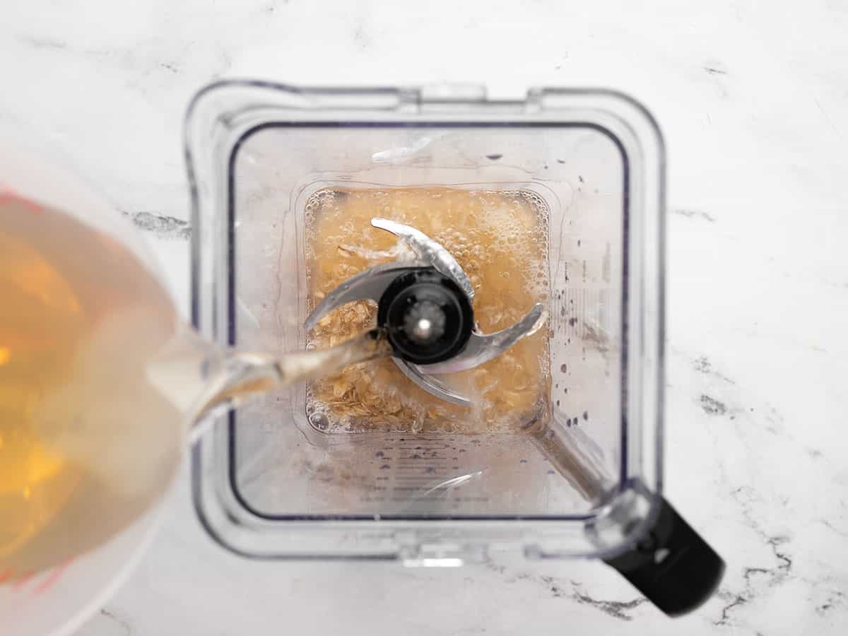 Maple water being poured into a blender with oats and salt.