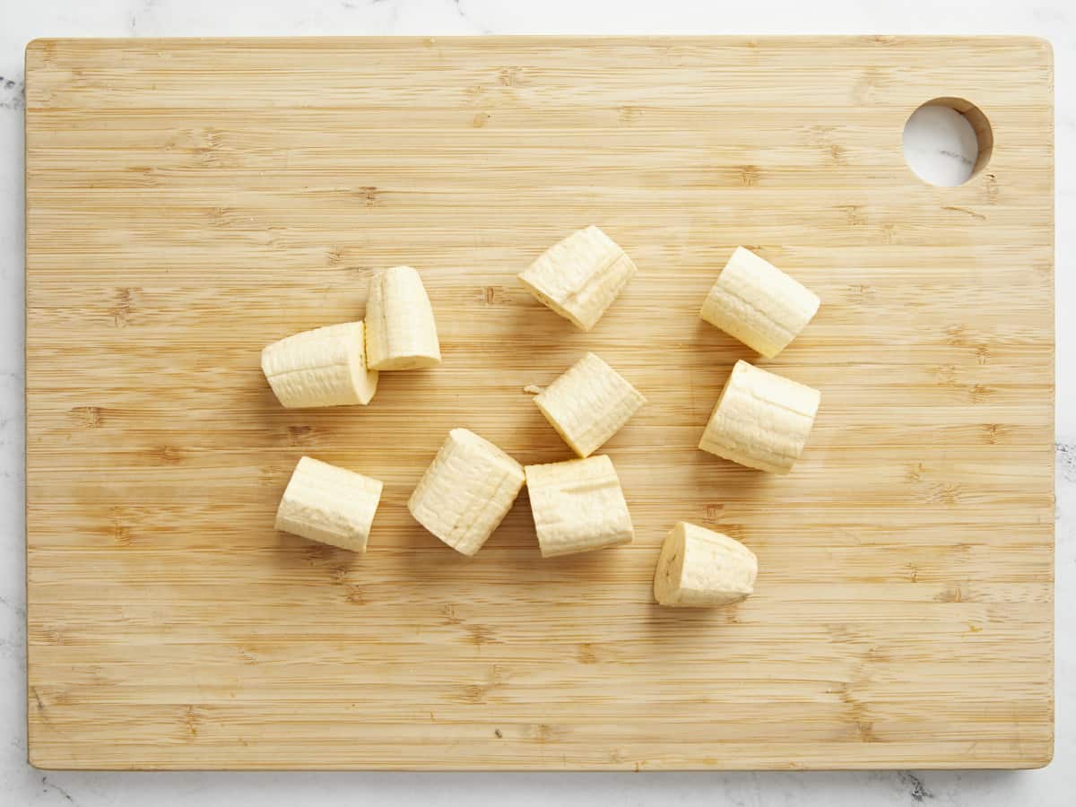 Overhead shot of slices of green plantain on a wood cutting board.