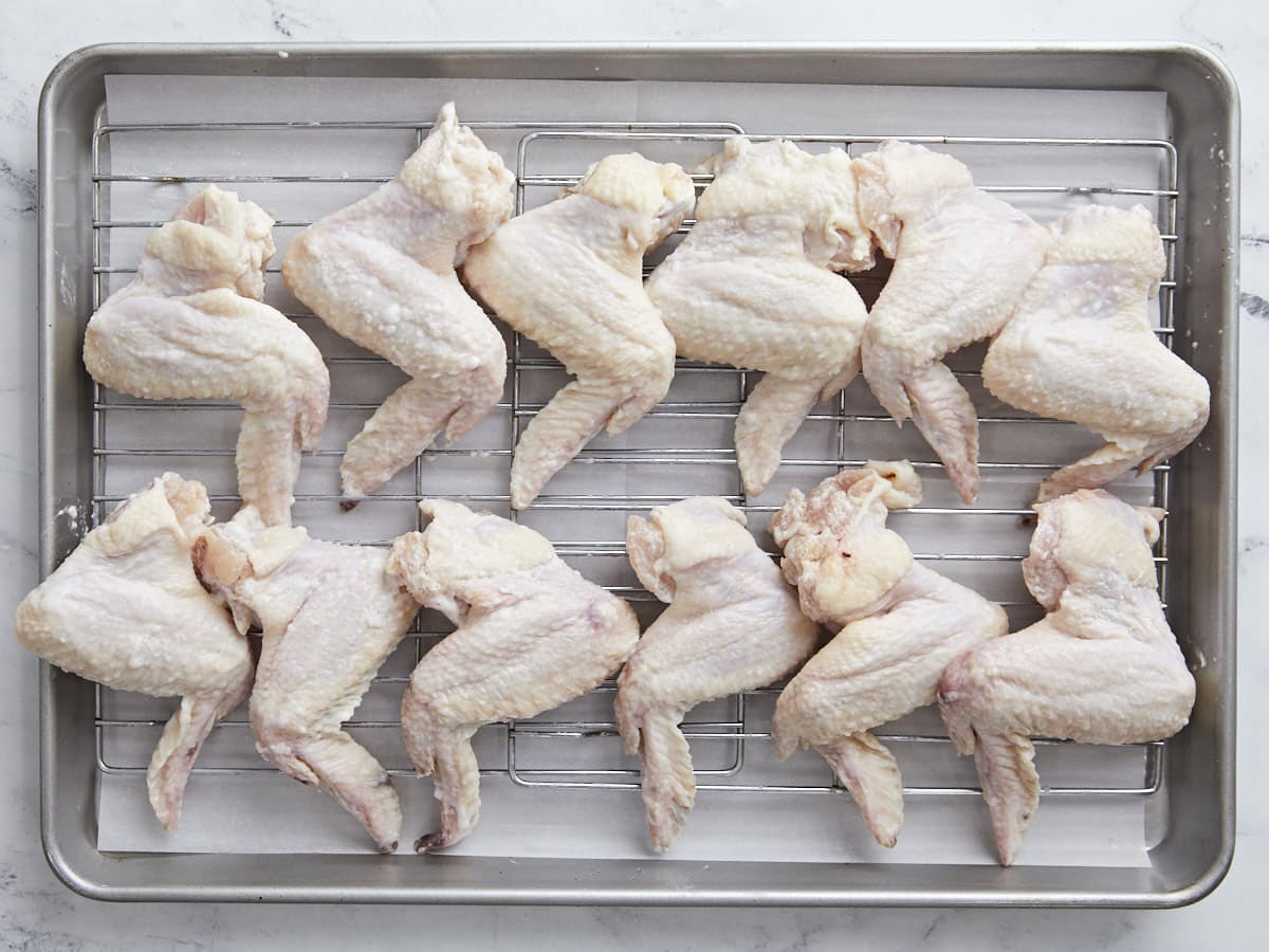 Overhead shot of chicken wings with baking powder and salt on a drying rack set over a sheet pan.