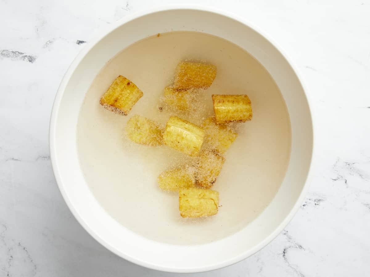 Overhead shot of slices of fried green plantain soaking in a salt water bath.