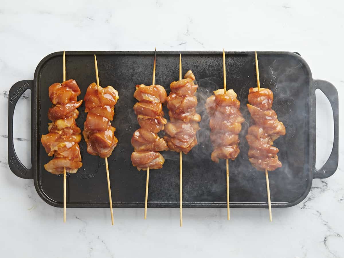 Overhead shot of Pinchos De Pollo cooking on a black grill plate.