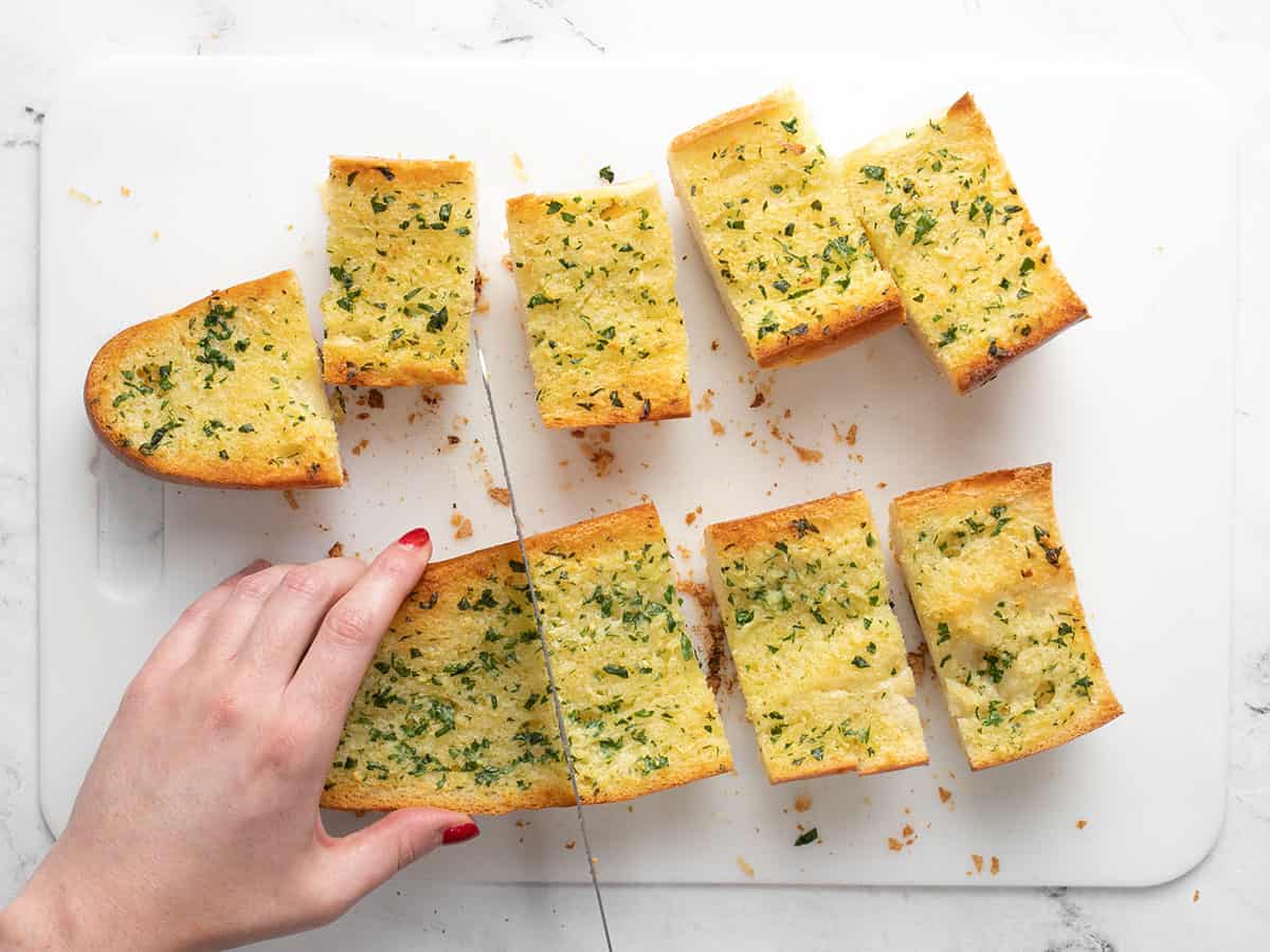 Garlic bread loaf being cut into pieces on a cutting board.