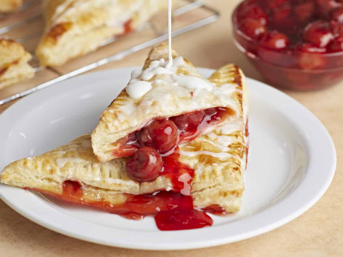 Icing being drizzled over two cherry turnovers on a plate.