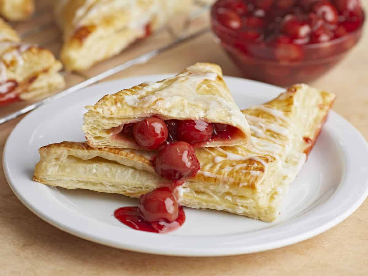 Two cherry turnovers stacked on a plate, one cut in half with filling spilling out.