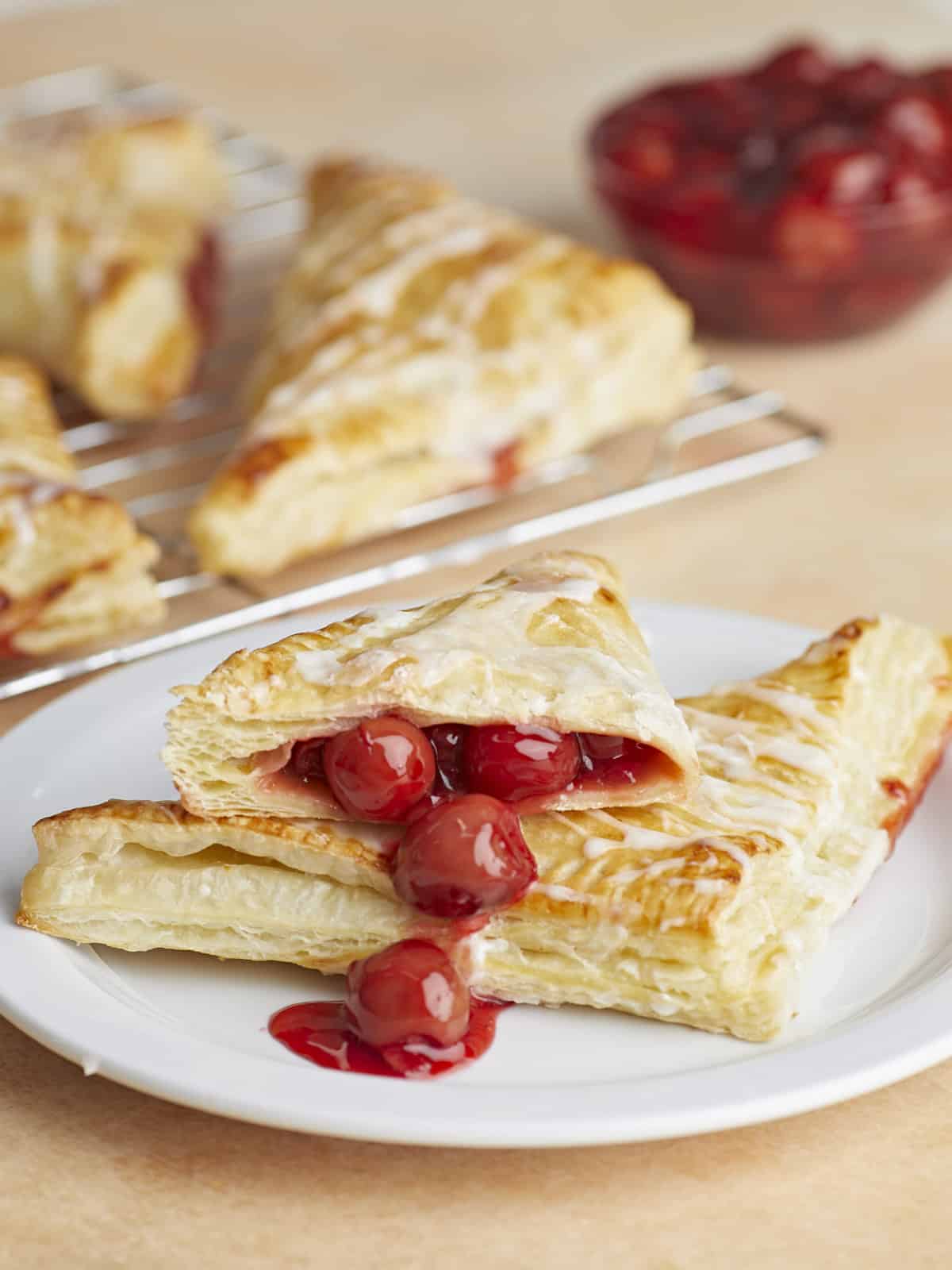 Two cherry turnovers on a plate, one cut in half with the filling dripping out.