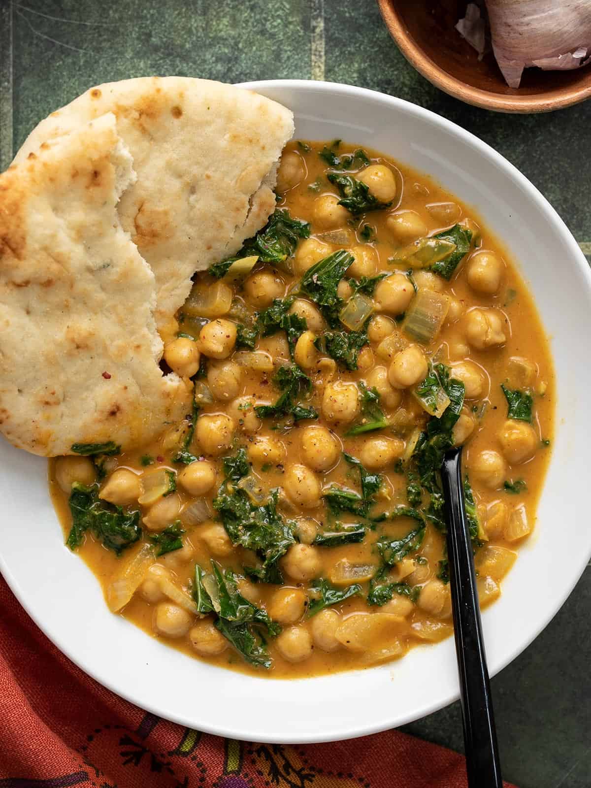 Close up overhead view of a bowl full of coconut curry chickpeas with naan bread on the side.