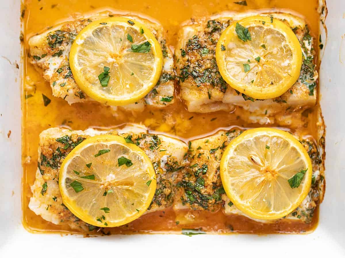 Overhead view of four cod filets in a baking dish with lemon.