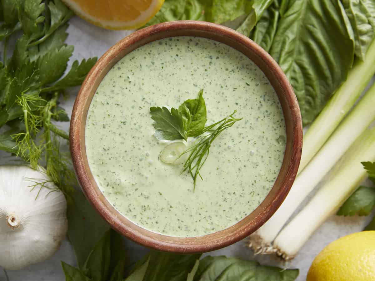 Overhead shot of Green Goddess Dressing in a wood bowl garnished with herbs.