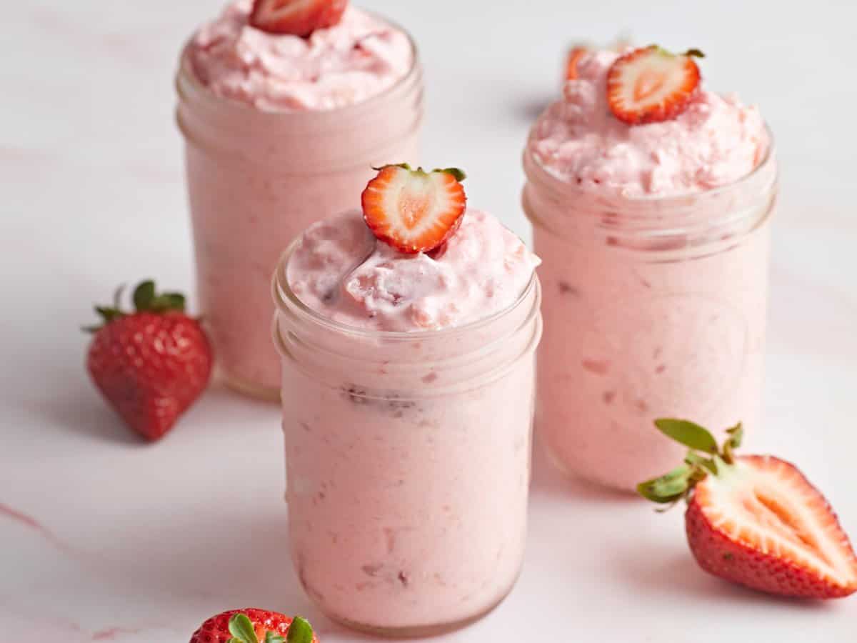 Jello salad in 3 mason jars with sliced strawberry on top.