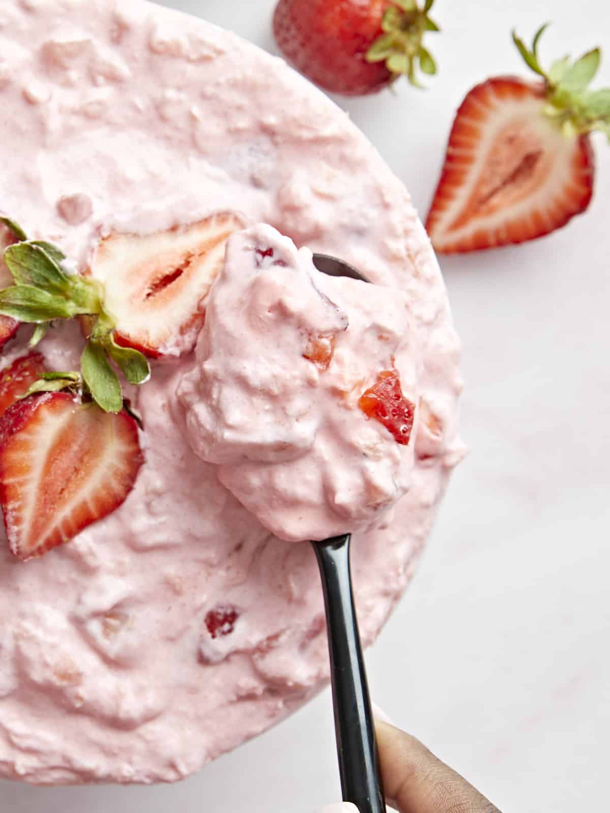 Overhead photo of a bowl of jello salad, topped with sliced strawberries and a spoon scooping a small serving out.