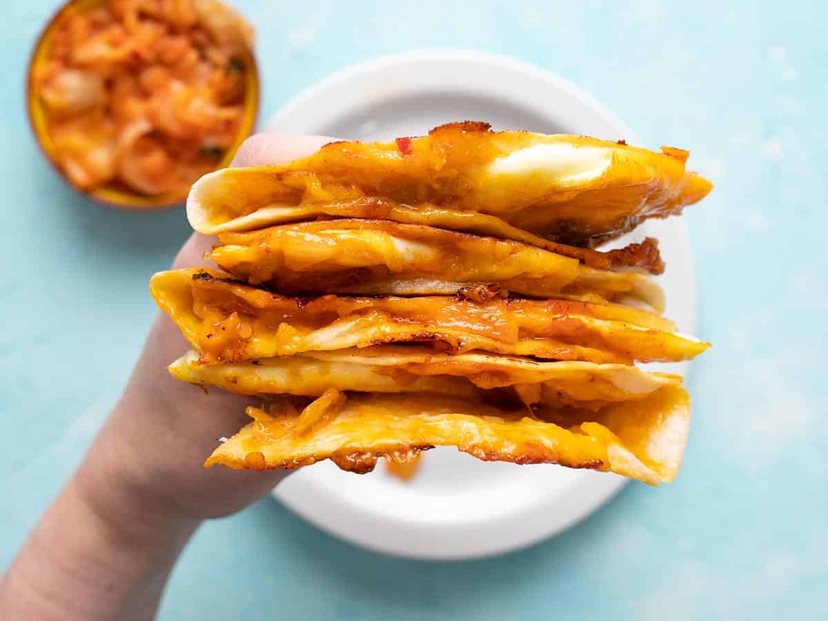 A hand holding a stack of kimchi quesadillas showing the cheese and filling.