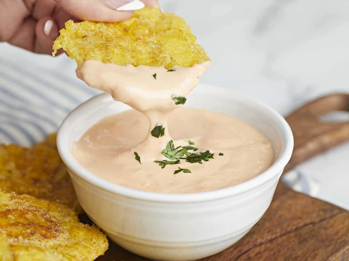 Side shot of toston being dipped in Mayo Ketchup in a small white bowl.