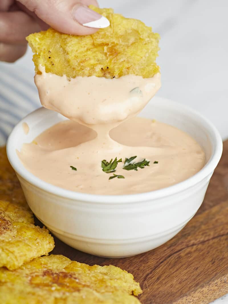 Side shot of toston being dipped in Mayo Ketchup in a small white bowl.