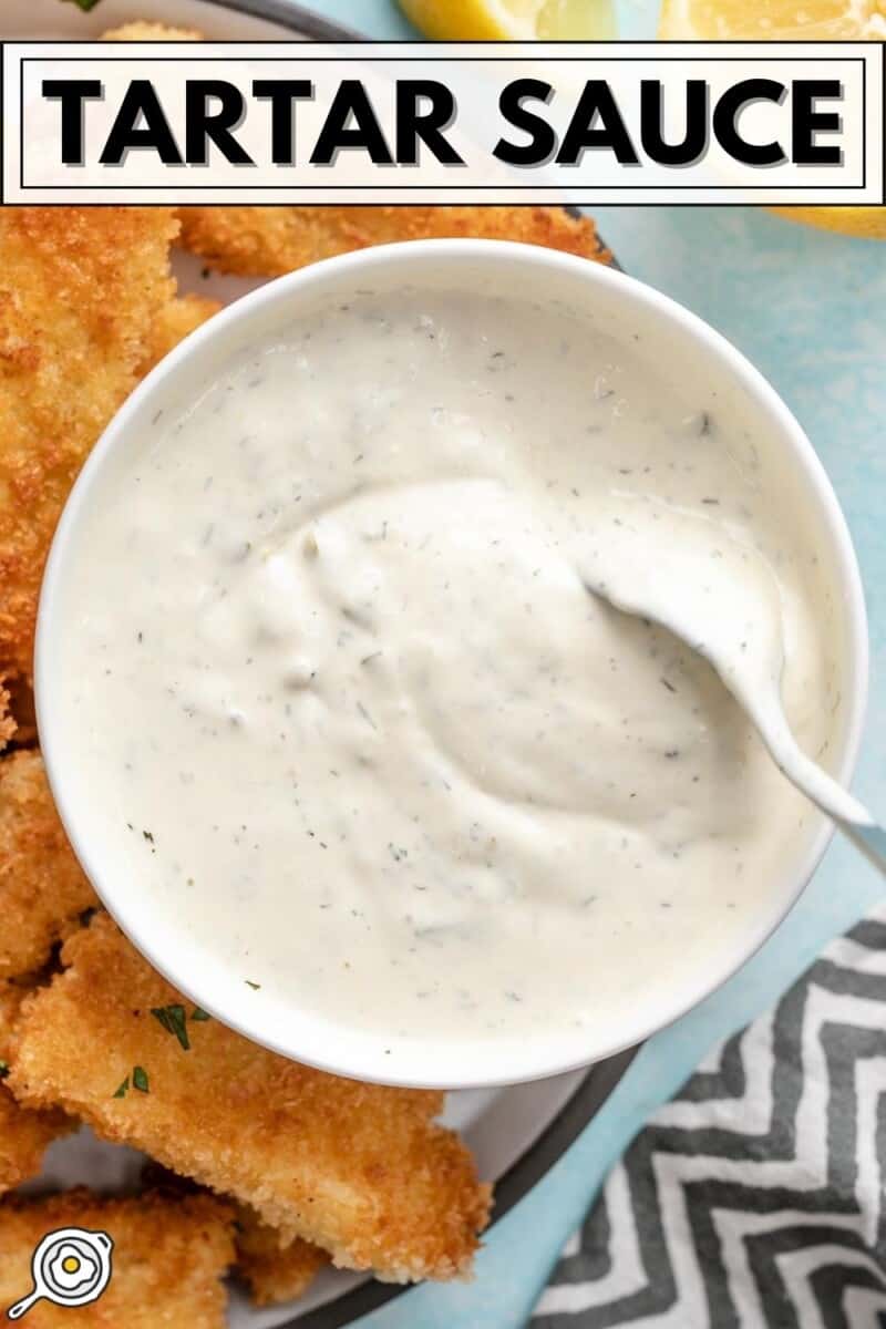 Overhead view of a bowl of tartar sauce being stirred with a spoon.