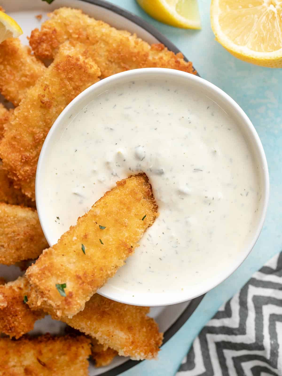 A fish stick being dipped into a bowl of tartar sauce.