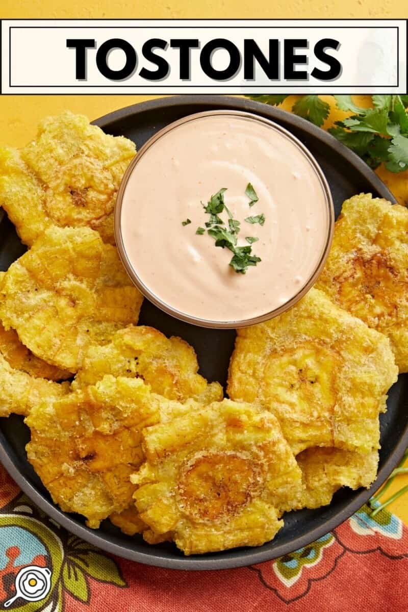 Overhead shot of fried tostones in a black bowl with mayo-ketchup sauce in the middle of the bowl.