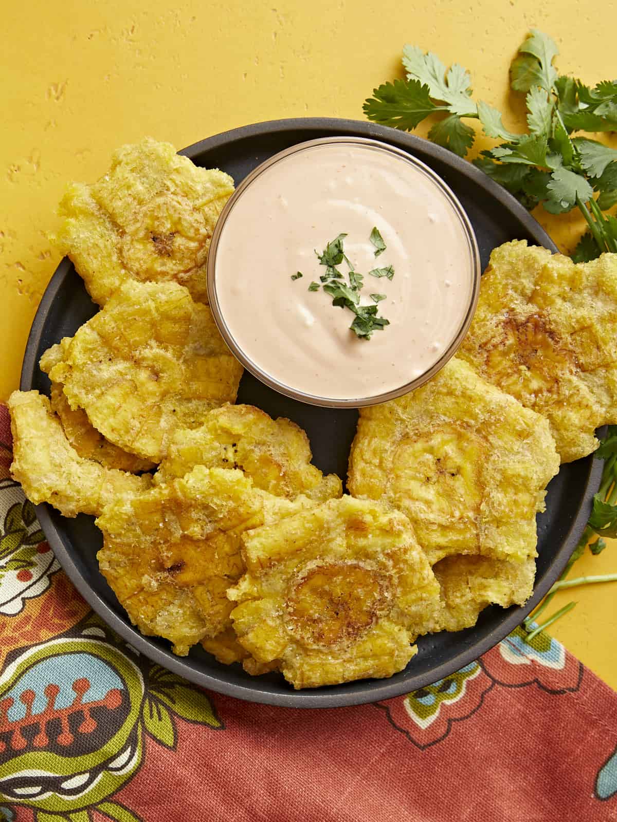 Overhead shot of fried tostones in a black bowl with mayo-ketchup sauce in the middle of the bowl.