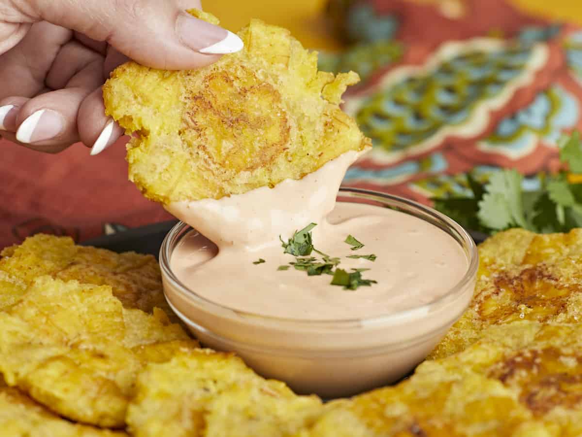 Side shot of a hand dipping a toston in mayo-ketchup sauce.