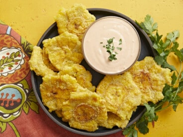 Overhead shot of fried tostones in a black bowl with mayo-ketchup sauce in the middle of the bowl.