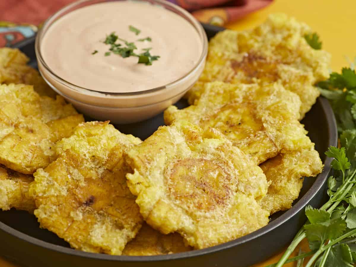 Side shot of fried tostones in a black bowl with mayo-ketchup sauce in the middle of the bowl.