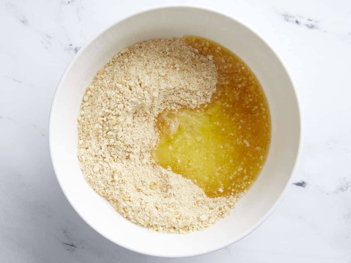 Melted butter added to crushed vanilla wafers in a bowl.