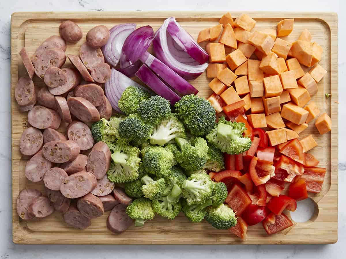 Ingredients sheet pan chicken sausage dinner chopped on a cutting board.