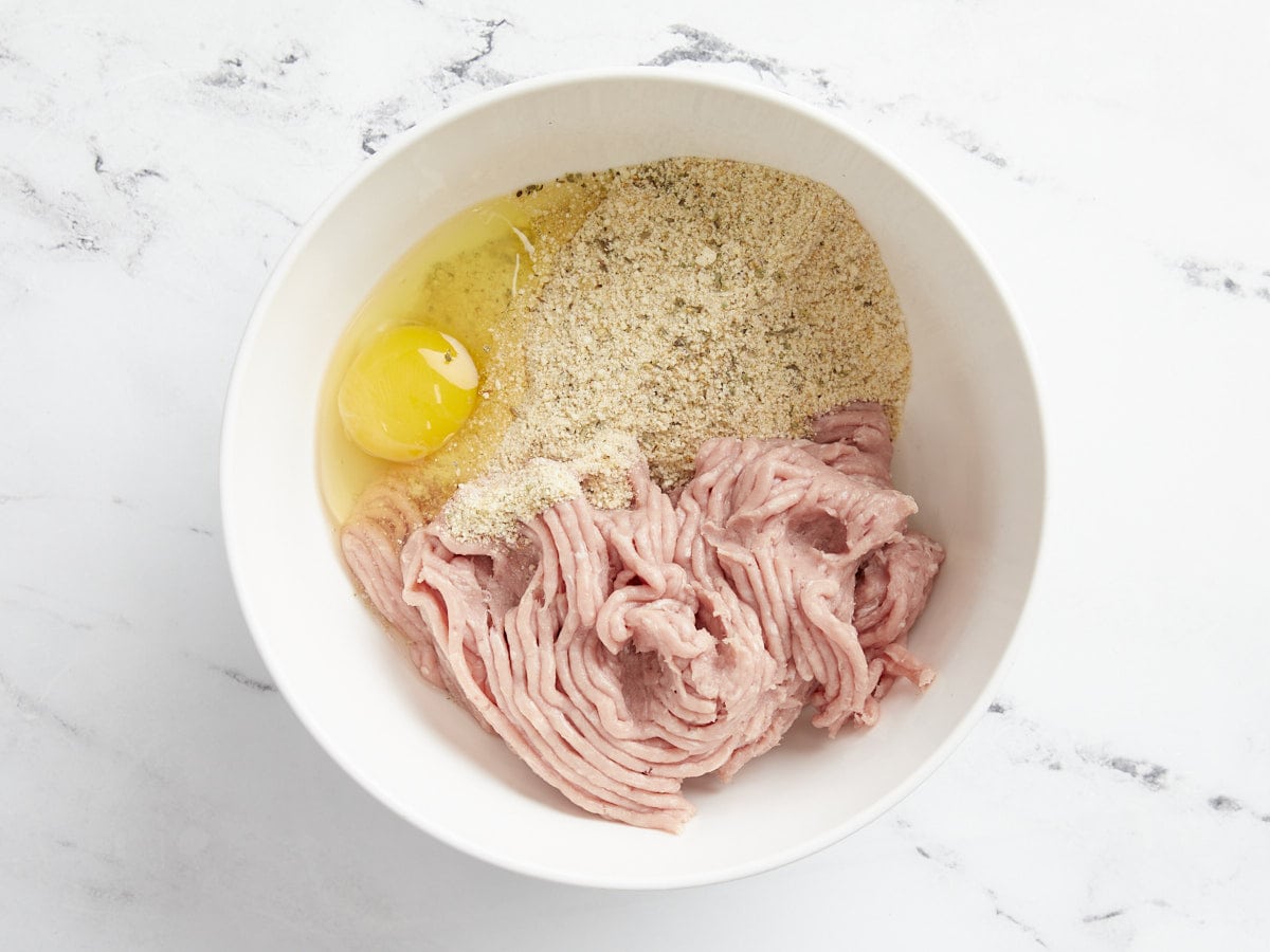 Ground turkey, egg, and breadcrumbs in a bowl, unmixed. 