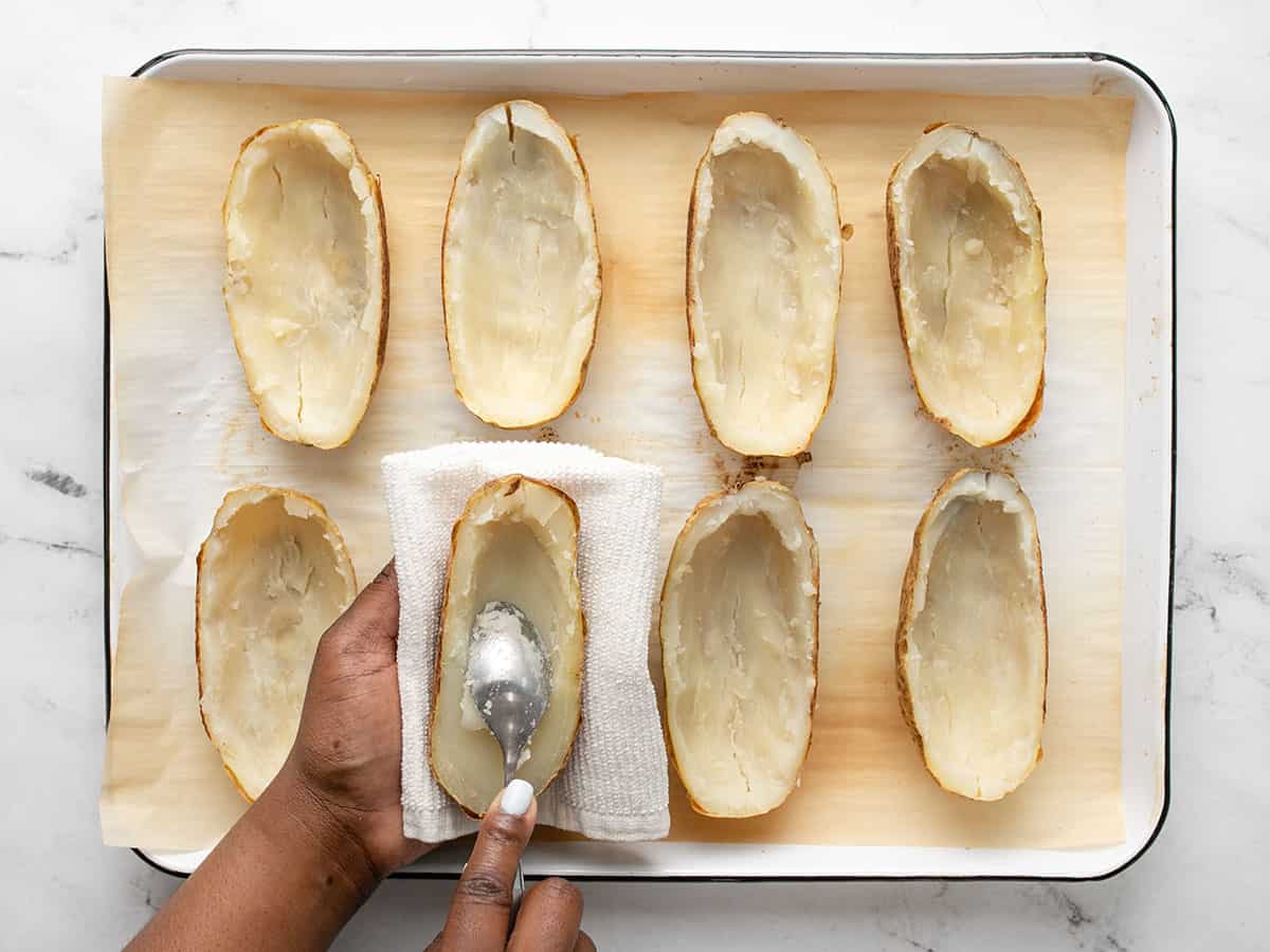 Cooked potatoes cut in half and flesh being scooped out.