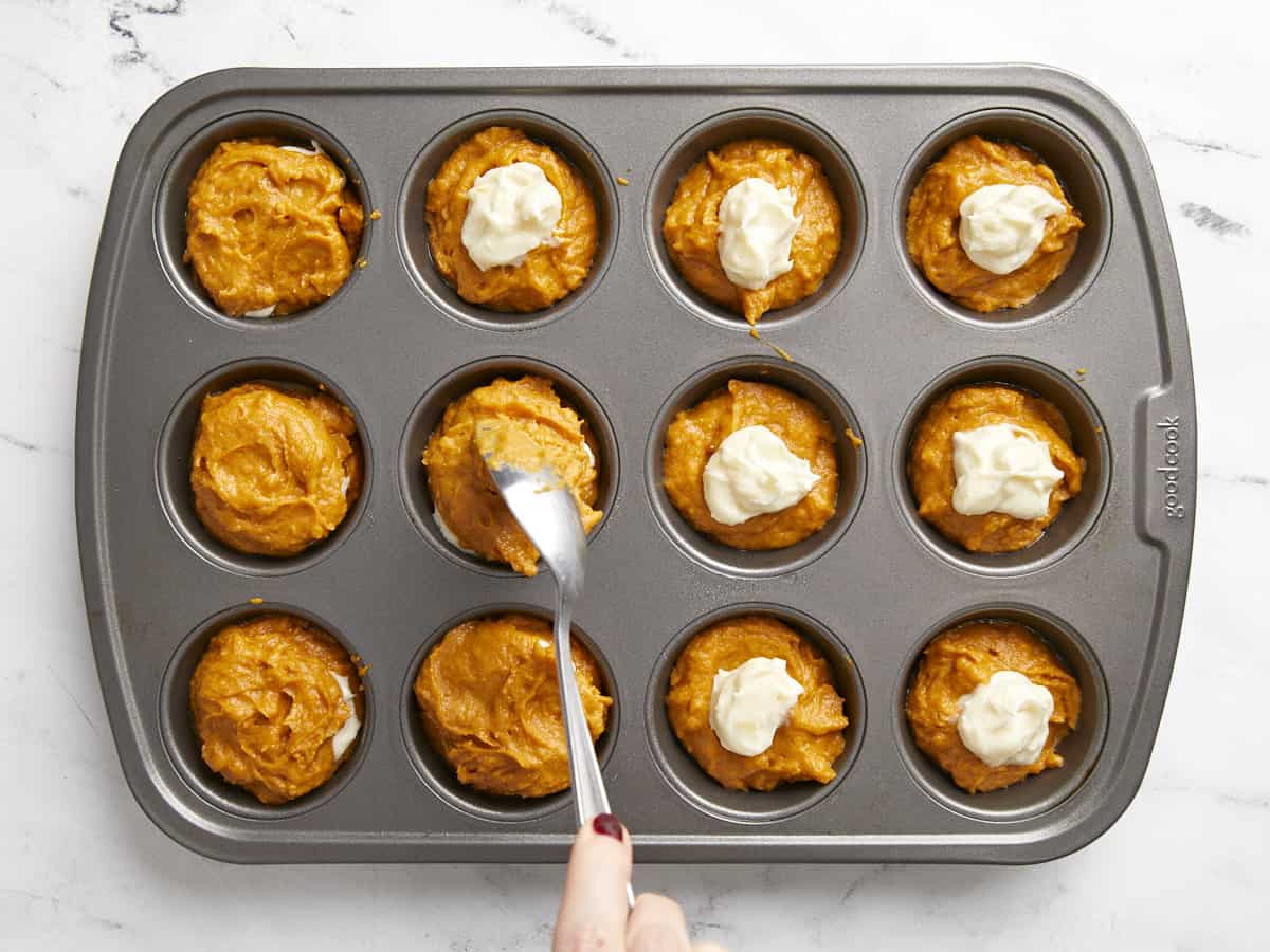 Muffin tin being filled with pumpkin batter and cream cheese filling.