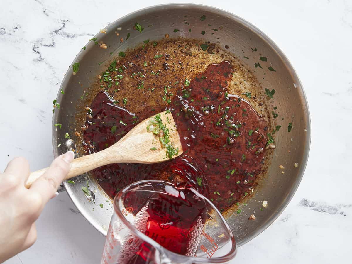 Red wine being poured into the pan to deglaze.