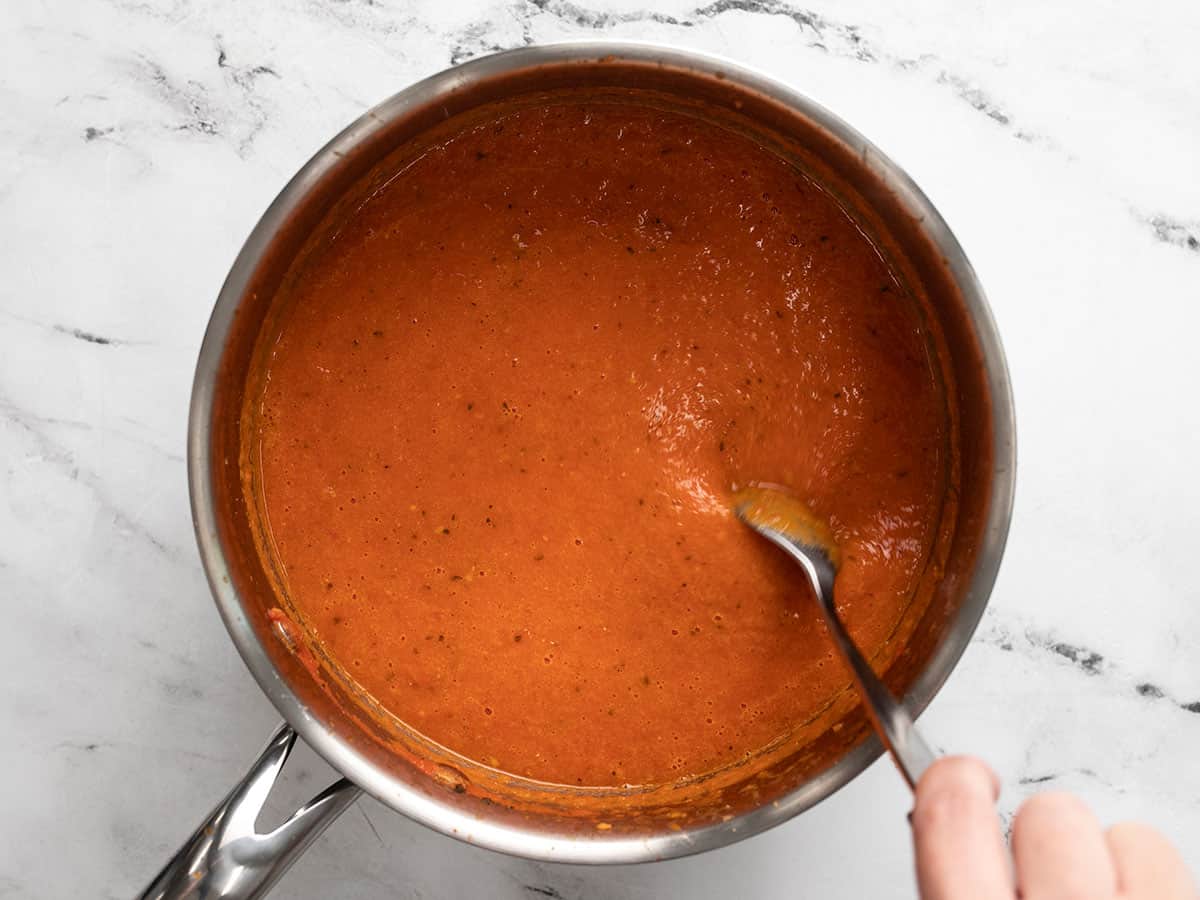 Finished roasted tomato soup in the soup pot being stirred with a spoon.