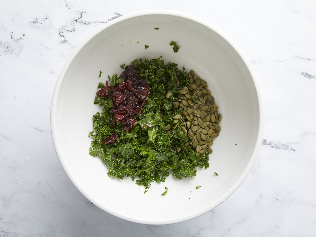 Cranberries and pepitas added to the kale in the bowl.