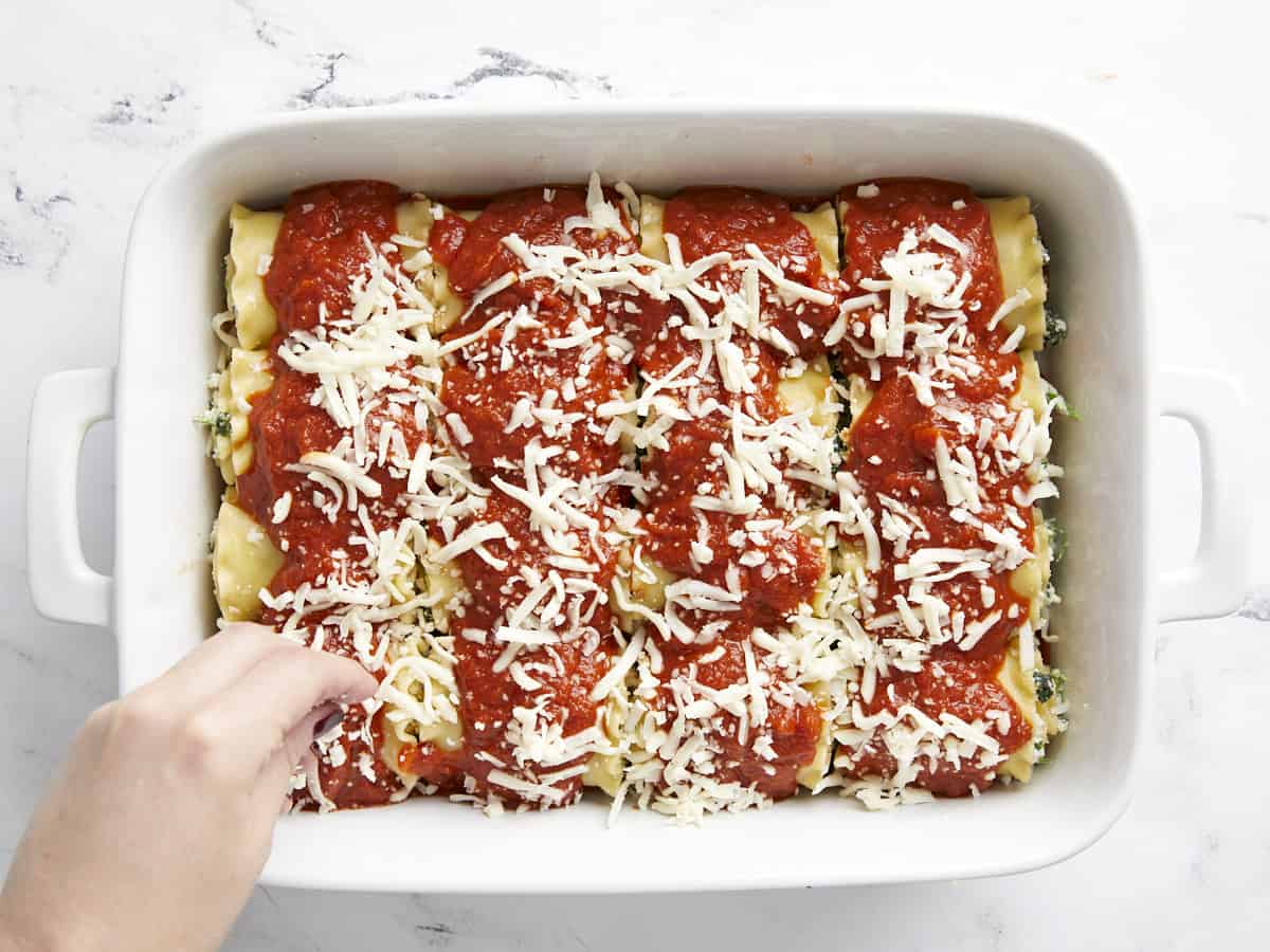 Cheese being sprinkled on top of the lasagna roll ups.