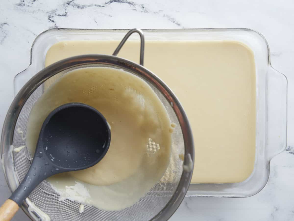 Coconut custard being strained through a sieve into the baking dish.