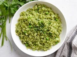 Overhead view of a white bowl full of Arroz Verde with parley and a grey napkin on the side.