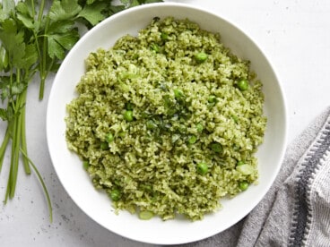 Overhead view of a white bowl full of Arroz Verde with parley and a grey napkin on the side.