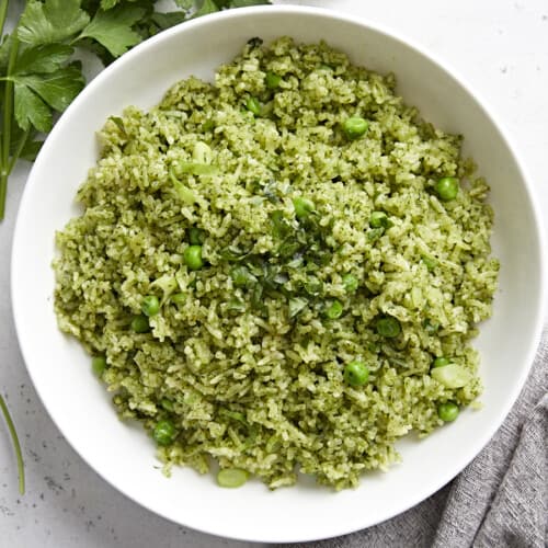 Overhead view of a white bowl full of Arroz Verde with parley and a grey napkin on the side.