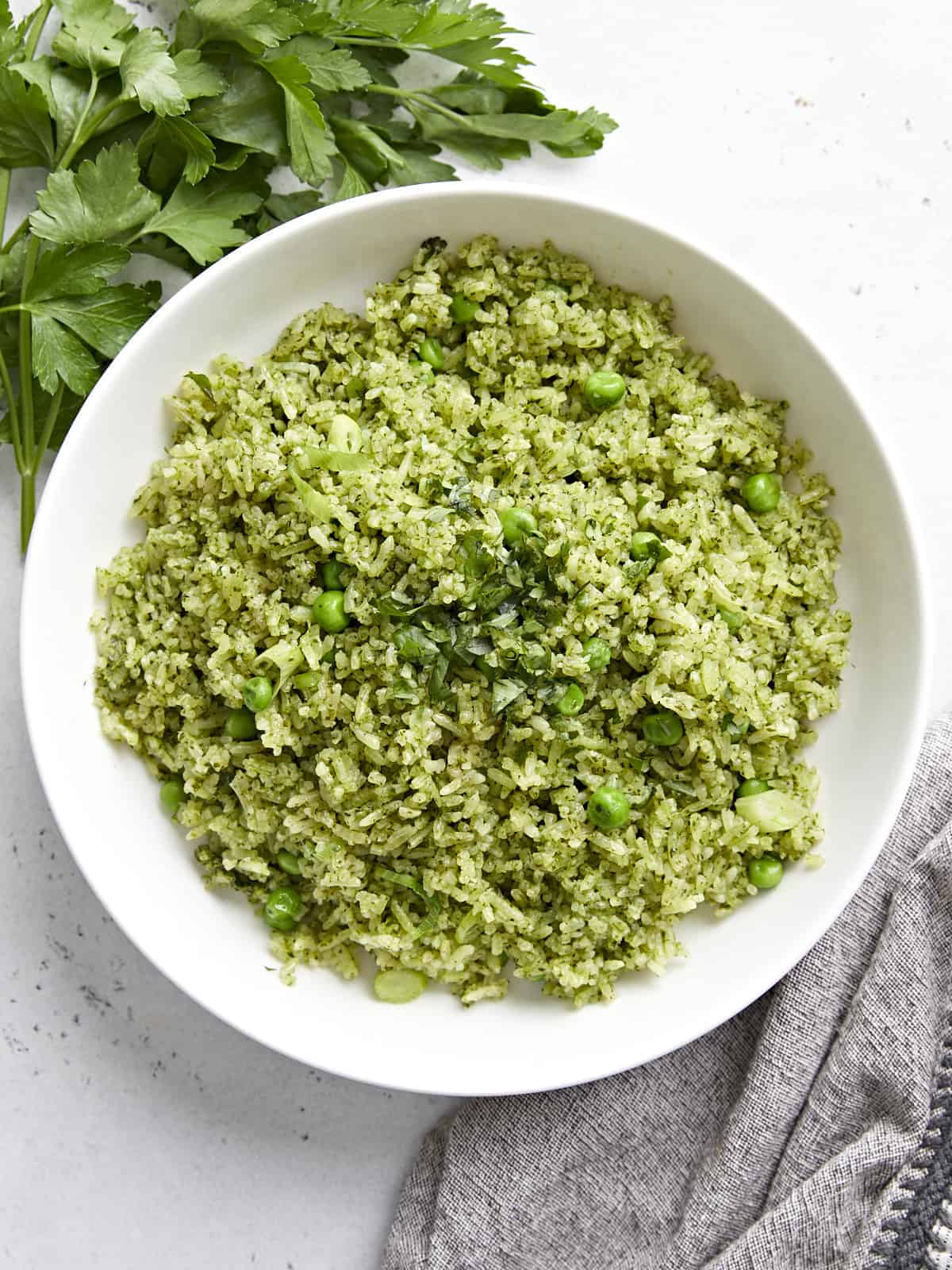 Overhead view of a white bowl full of Arroz Verde with parley and a grey napkin on the side.