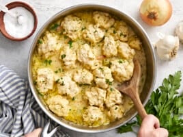 Chicken and dumplings in the skillet being scooped out with a spoon.