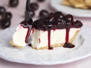 Side view of one slice of no bake cheesecake on a plate, a fork taking a bite.