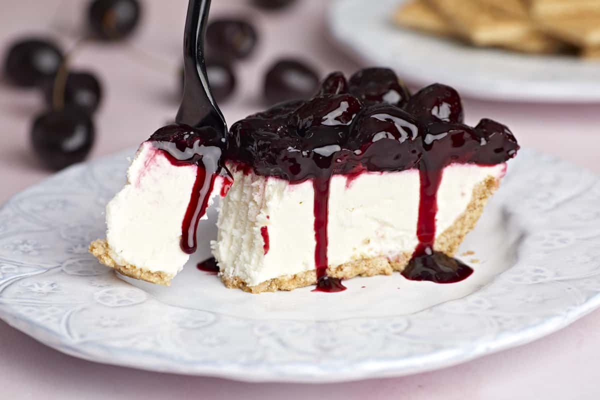 Side view of one slice of no bake cheesecake on a plate, a fork taking a bite.