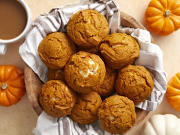 Overhead view of a basket full of pumpkin muffins with coffee and pumpkins on the sides.