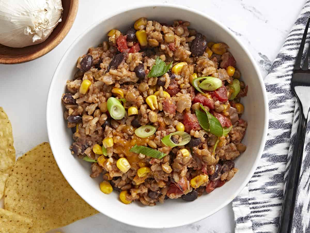 Overhead view of a white bowl full of southwest lentils and rice with tortilla chips, a napkin, and black fork on the side.