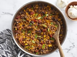 Overhead shot of southwest lentils and rice skillet garnished with green onions and a wooden spoon placed inside the skillet.